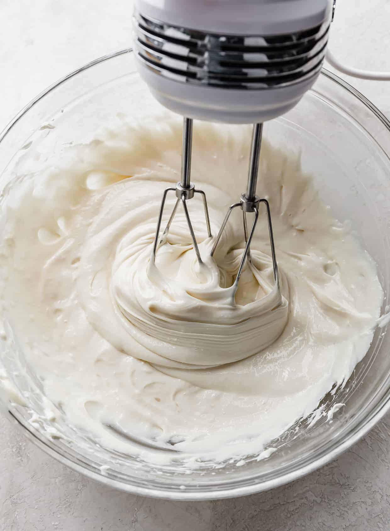 Hand beaters mixing no-bake cheesecake filling in a glass bowl.