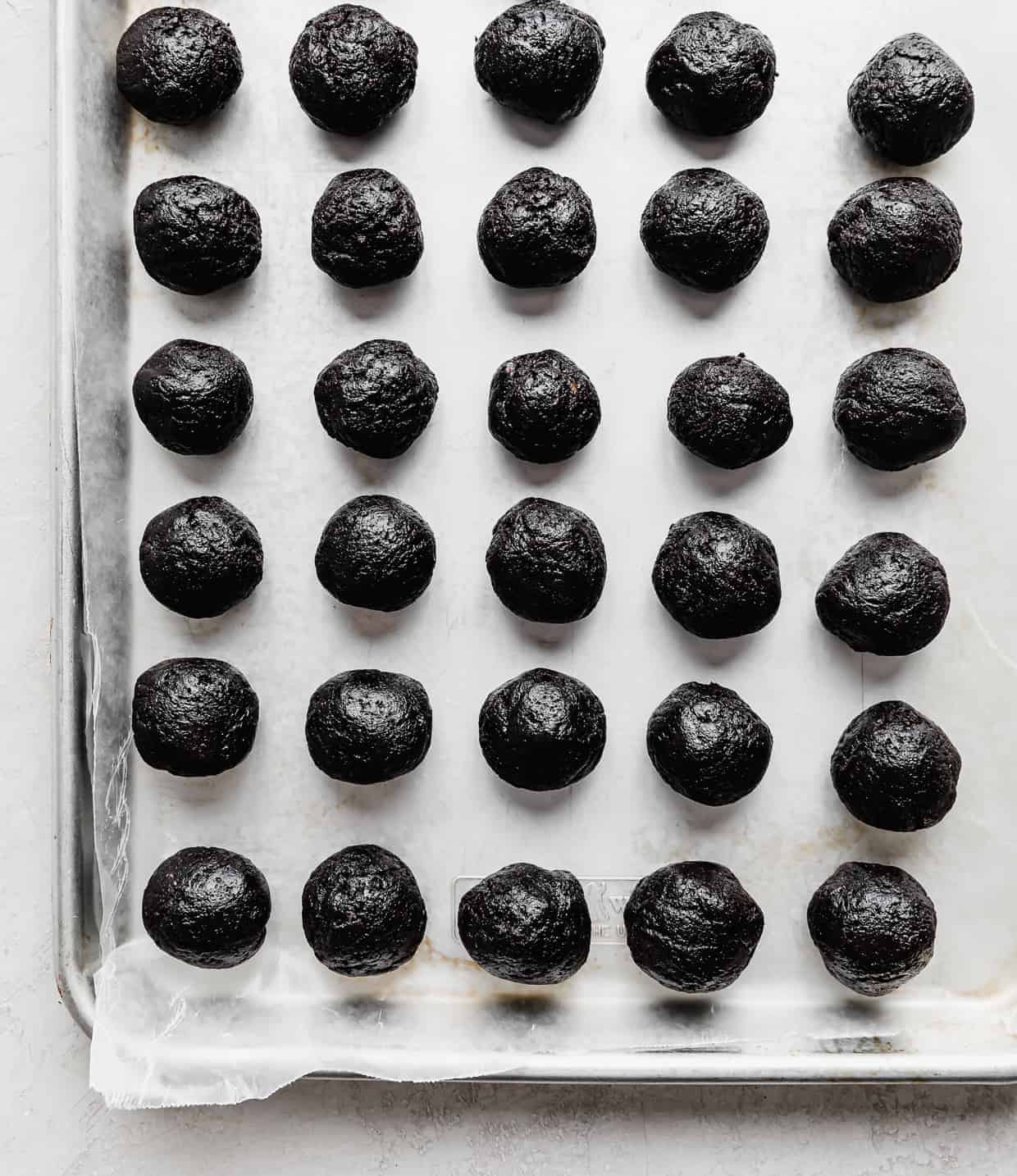 A wax paper lined baking sheet with round Oreo balls lined up on the sheet.