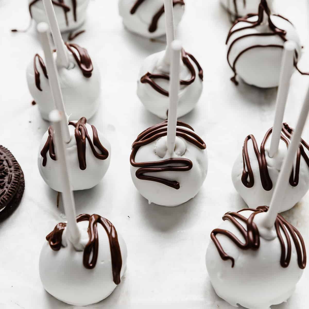 White chocolate covered Oreo Pops with brown chocolate drizzled overtop.