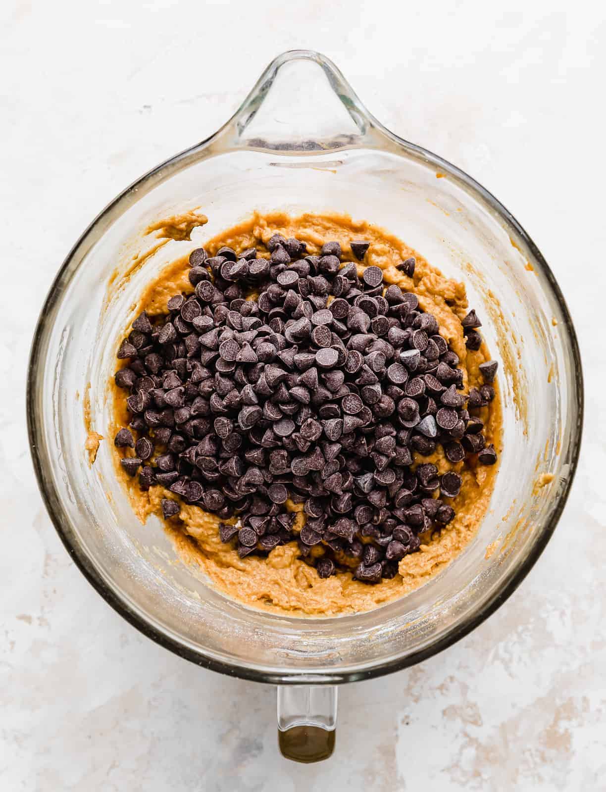 Chocolate chips in a glass bowl atop an orange cake batter mixture.