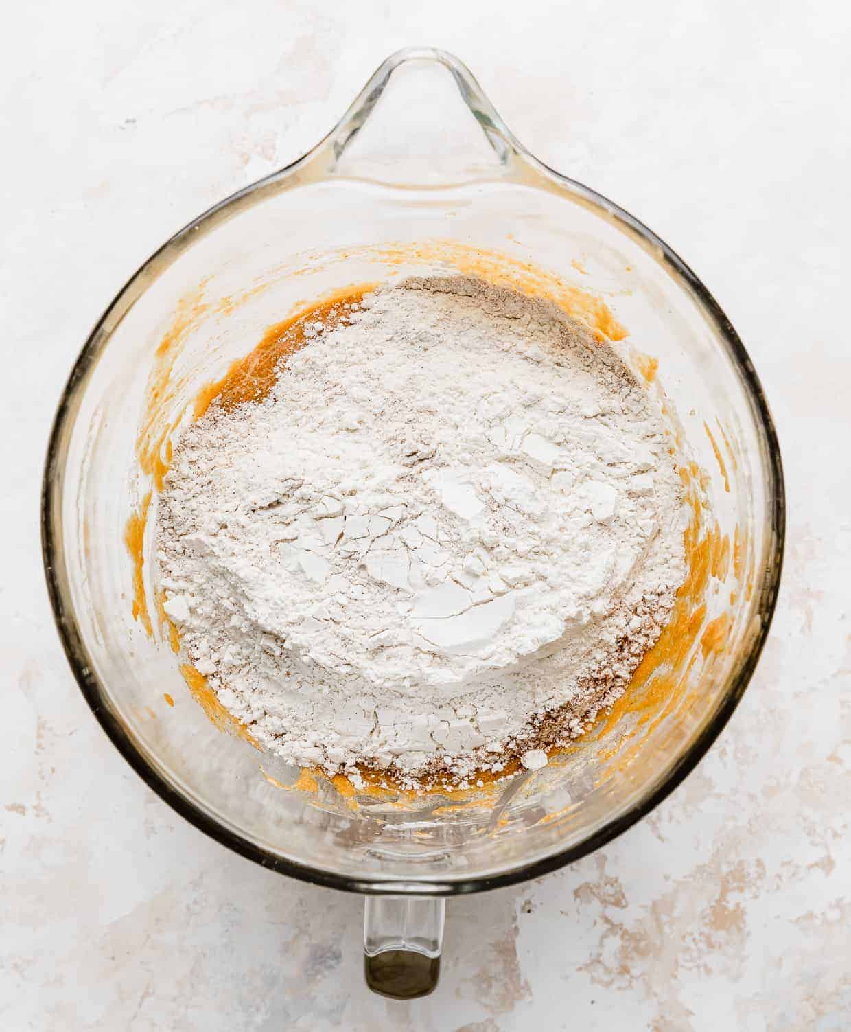 Dry ingredients a top an orange batter in a glass bowl.