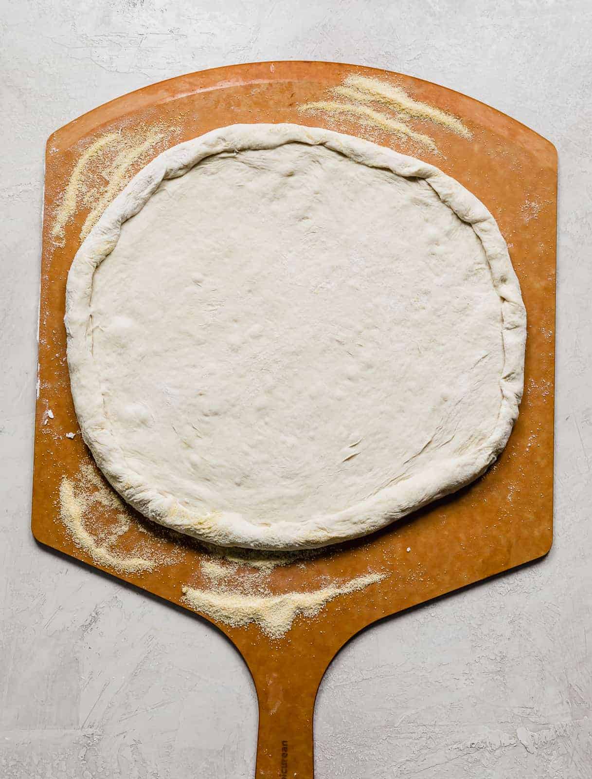 A pizza peel with a round pizza dough spread on it.