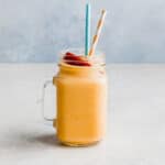 A glass cup filled with a banana peach smoothie mixture and two straws.