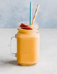 A glass cup filled with a banana peach smoothie mixture and two straws.