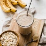 A Lactation Smoothie on a small wooden cutting board with ripe bananas in the background.
