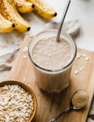 A Lactation Smoothie on a small wooden cutting board with ripe bananas in the background.