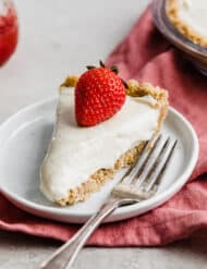 A no-bake cheesecake on a white plate topped with a red strawberry.