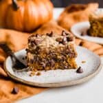 A slice of pumpkin chocolate chip coffee cake on a plate with an orange pumpkin in the background.