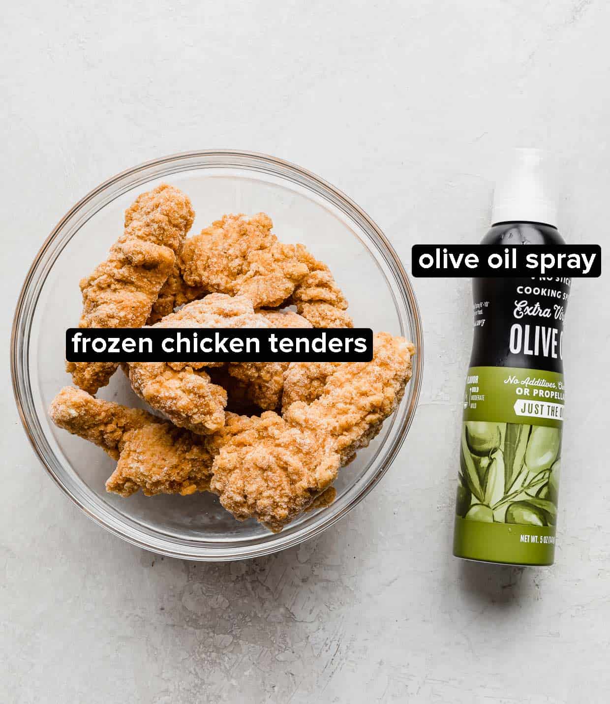 A glass bowl with frozen chicken tenders in it with a green bottle of olive oil spray next to it.