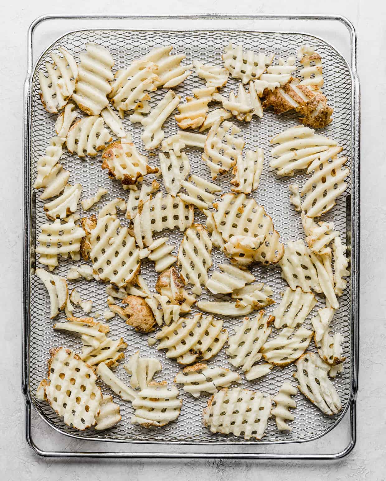 A wire air fryer rack with frozen waffle fries on it.