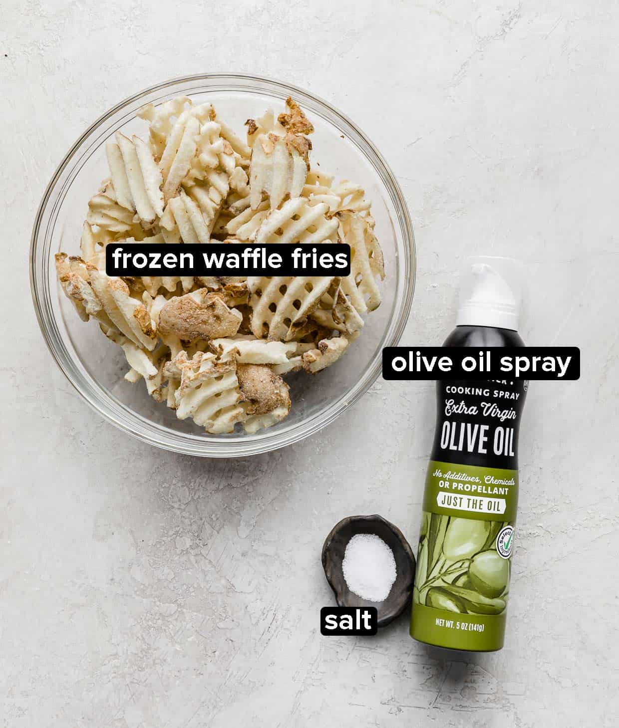 Frozen waffle fries in a glass bowl with a bowl of salt and olive oil spray next to the bowl.