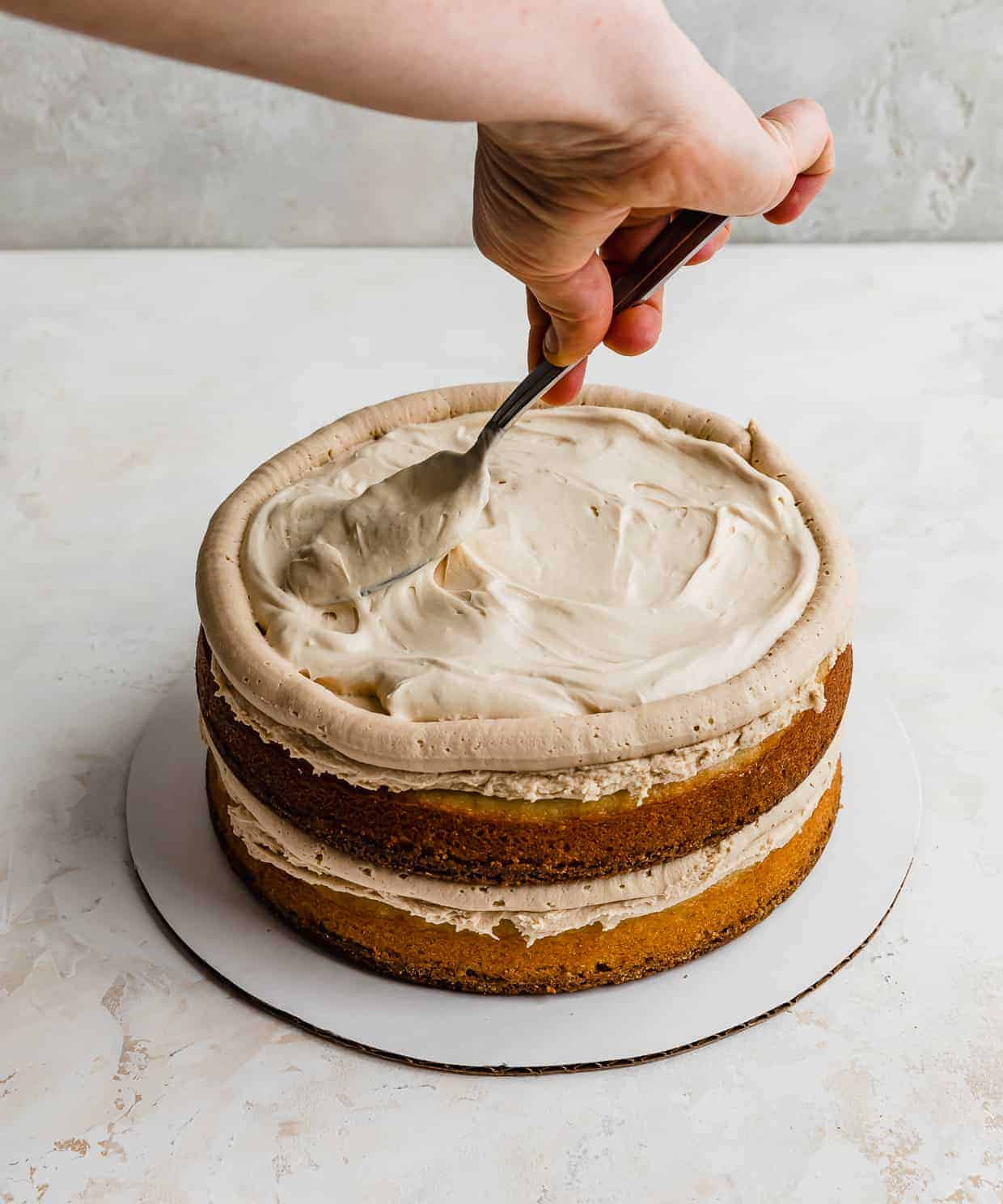 A spoon spreading a tan colored caramel filling on top of a cheesecake cake layer.