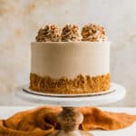 A Biscoff Caramel Cake on a marble cake stand against a cream colored background.