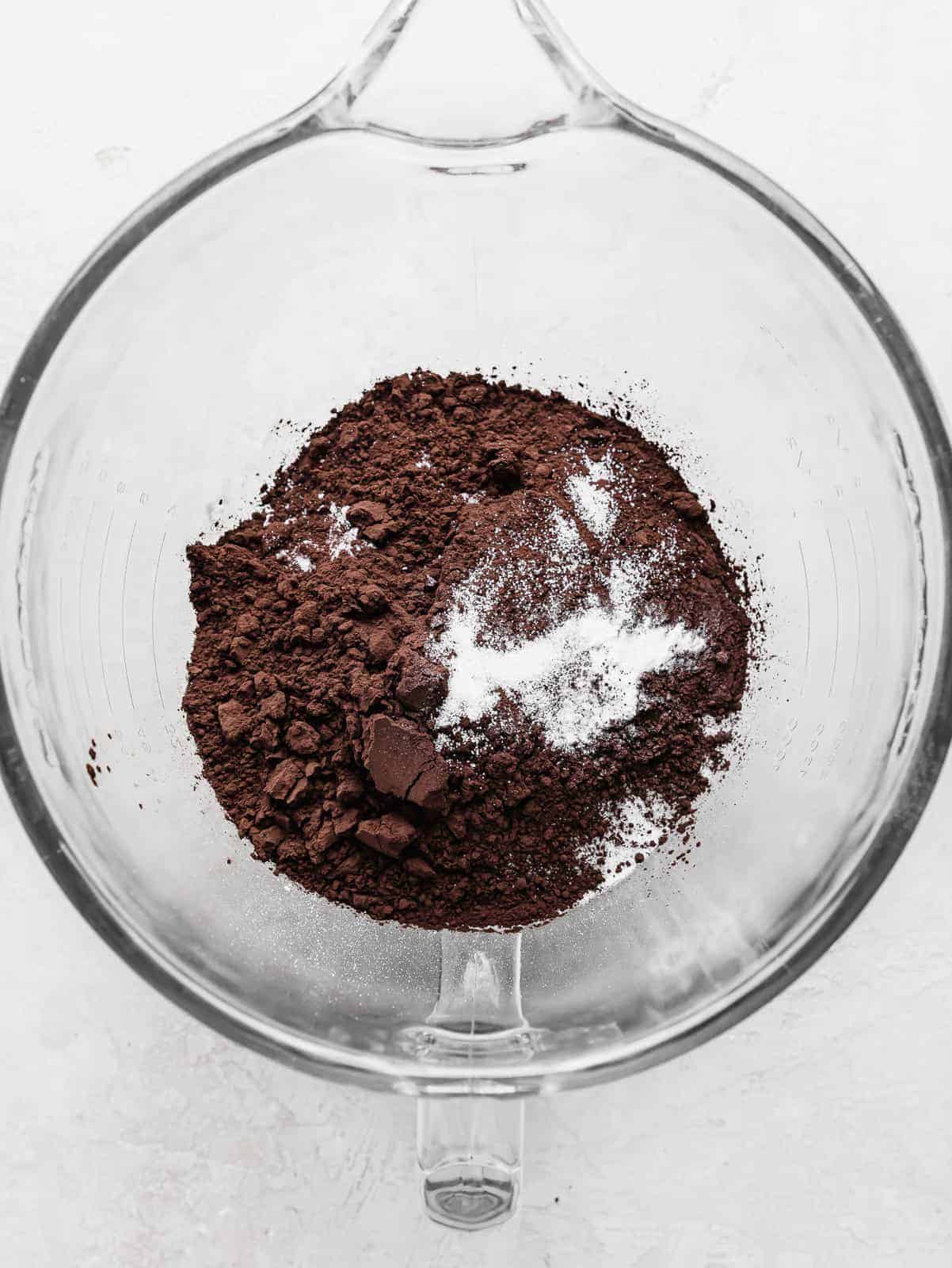 A glass mixing bowl with black cocoa, flour, salt, and baking soda in it.