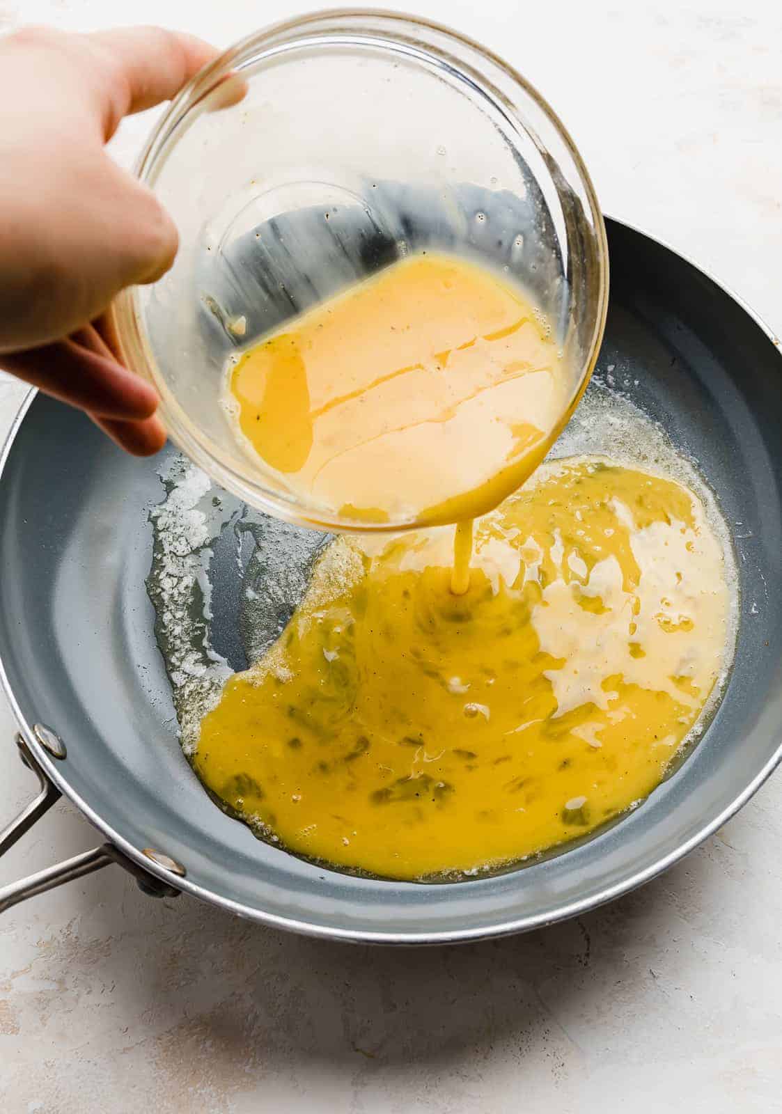 A whisked egg mixture being poured into a gray skillet.