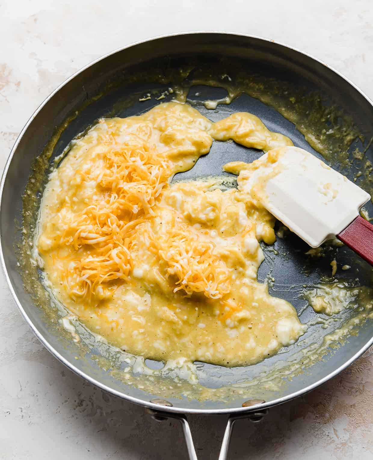 Shredded cheddar cheese overtop scrambled eggs in a skillet.
