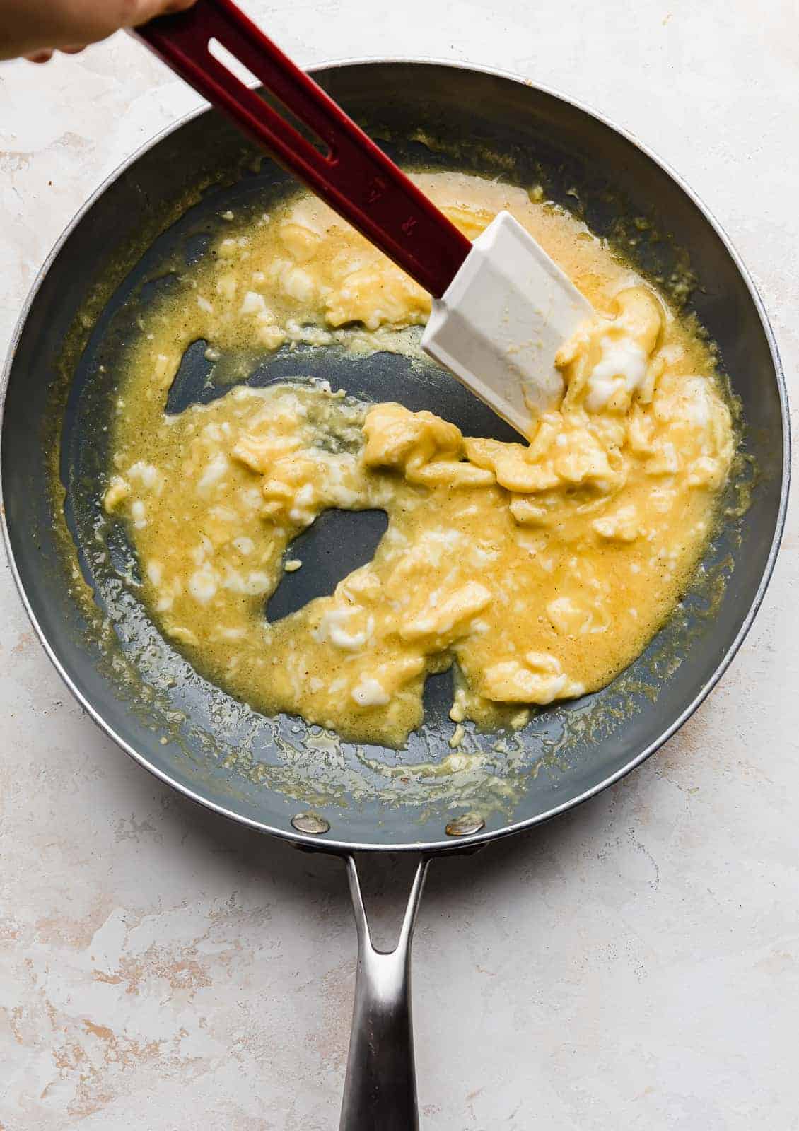 A spatula stirring a scrambled egg mixture in a skillet.