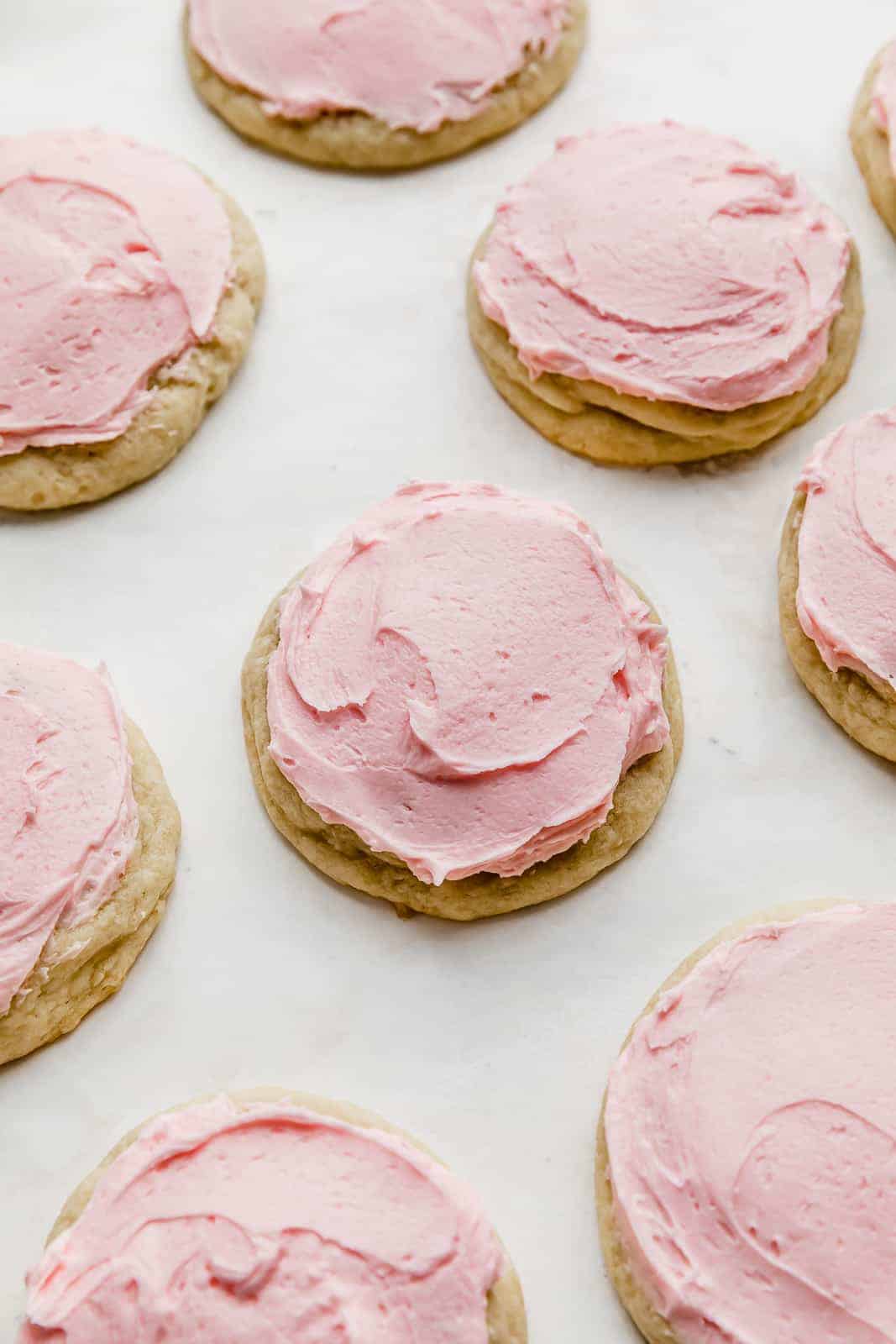A Copycat crumbl sugar cookie topped with pink frosting on a white background.
