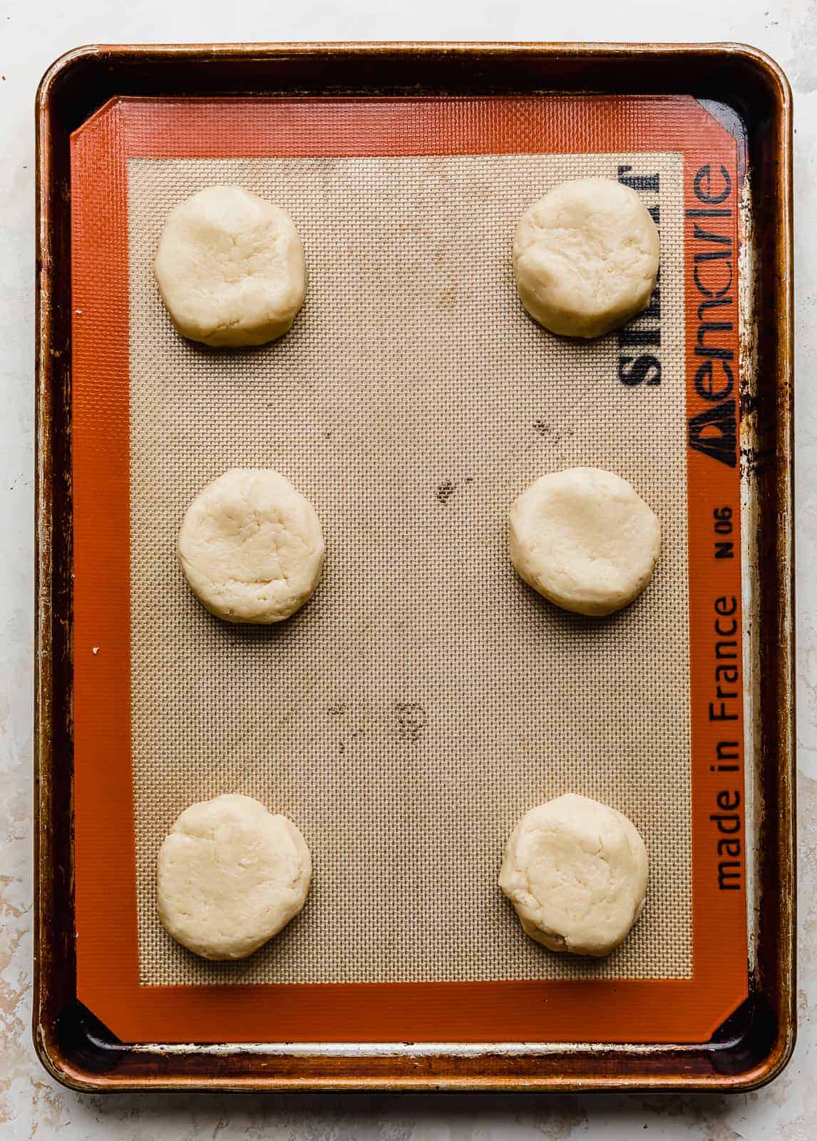 Six sugar cookie dough balls on a baking sheet.