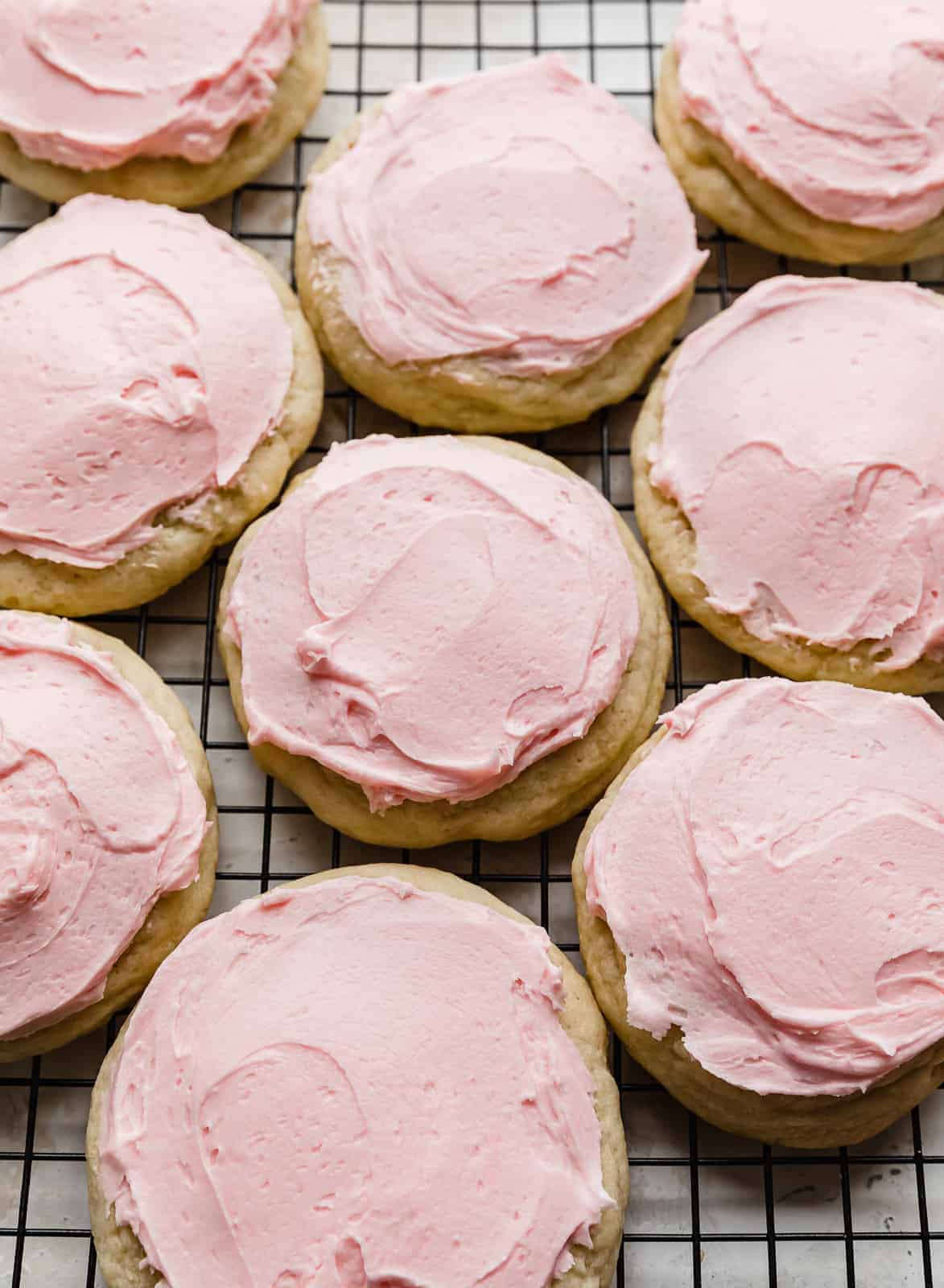 Copycat Crumbl Sugar Cookies topped with a pink frosting, on a black wire cooling rack.