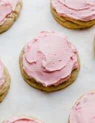 A Copycat crumbl sugar cookie topped with pink frosting on a white background.