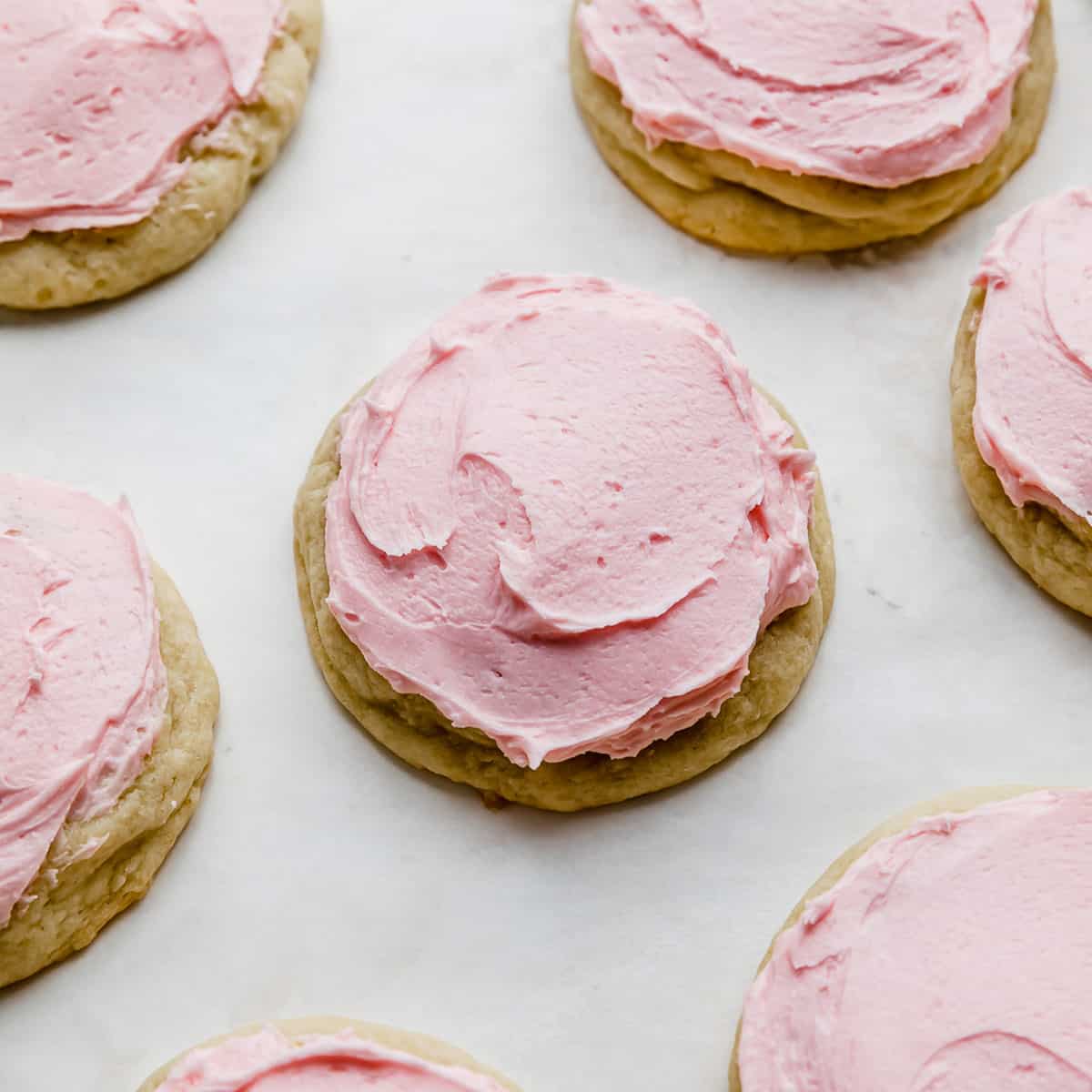 A Copycat crumbl sugar cookie topped with pink frosting on a white background.