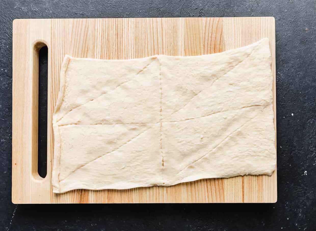 A wooden cutting board with an unrolled crescent roll sheet on it.