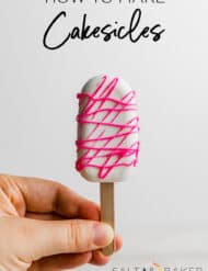 A hand holding a Cakesicle that has been covered in white chocolate and drizzled with hot pink chocolate.