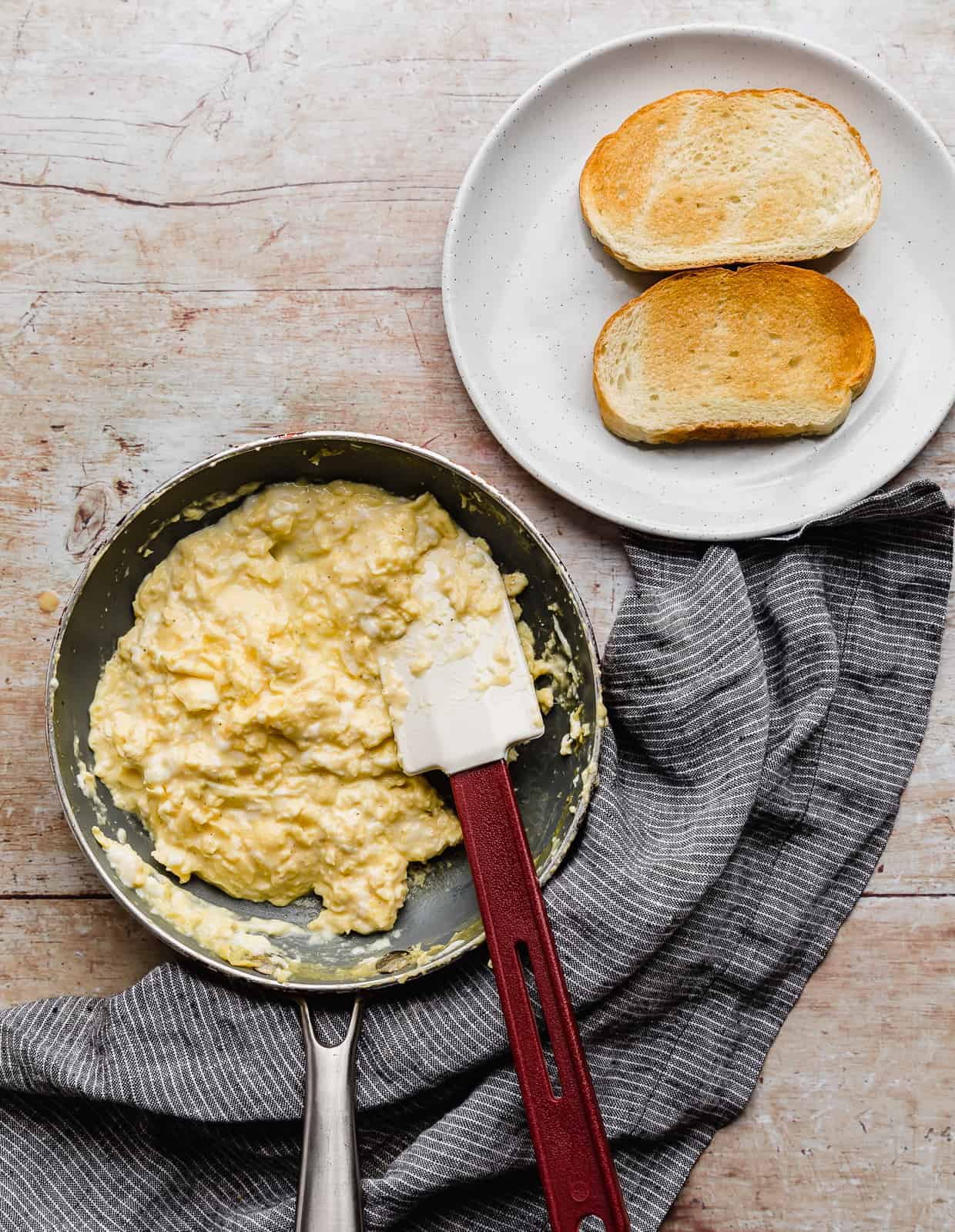 A skillet with scrambled eggs in it, and a plate with 2 toasted slices of bread on it. 