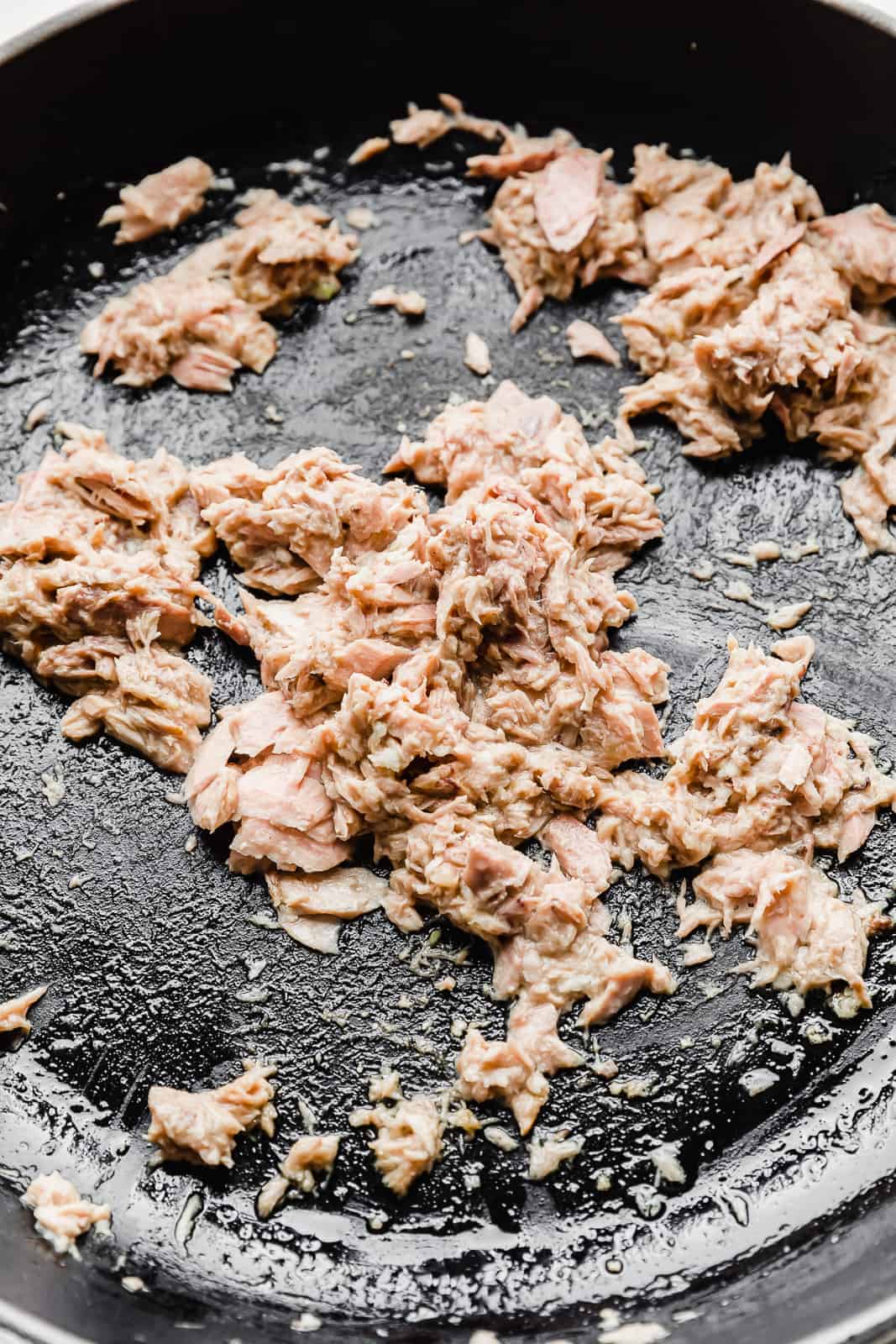 Canned tuna being cooked in a black skillet.
