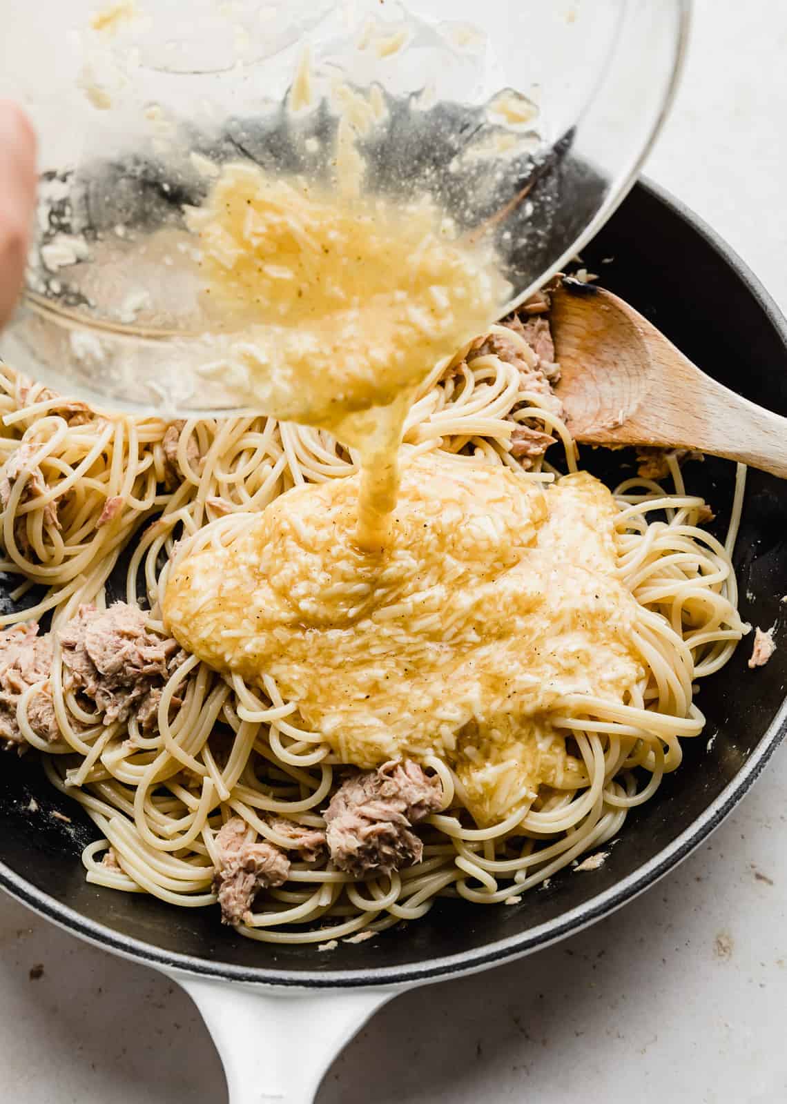 A yellow egg and cheese mixture being poured overtop of spaghetti noodles and tuna. 