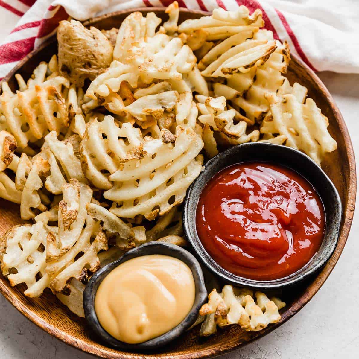Waffle fries on a brown plate with bowls of ketchup and chick fil a sauce beside them.