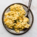 A gray plate full of Cheesy Scrambled Eggs that have been garnished with fresh parsley.
