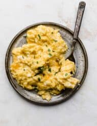 A gray plate full of Cheesy Scrambled Eggs that have been garnished with fresh parsley.