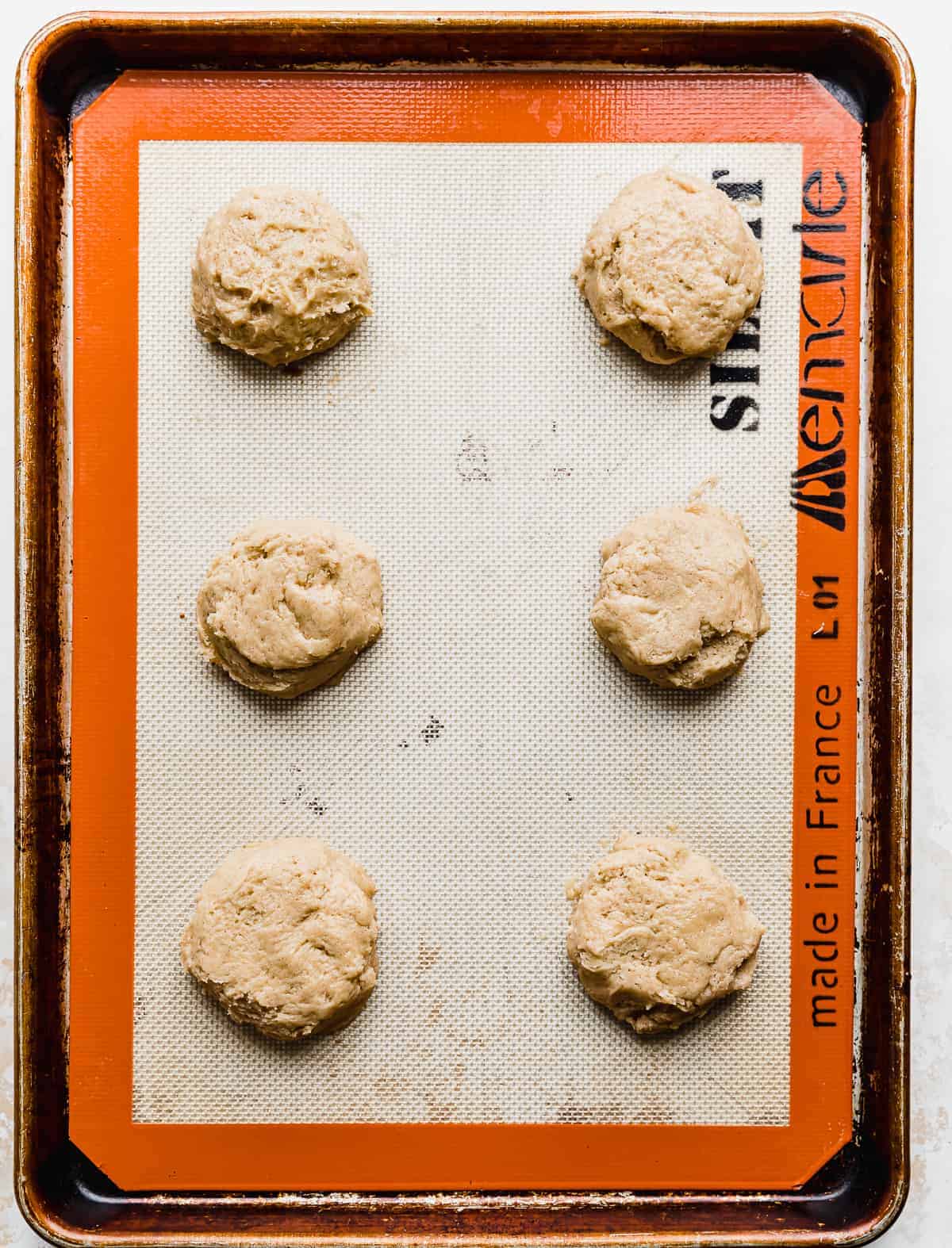 A baking sheet with six unbaked Caramel Apple Cookie dough balls on it.
