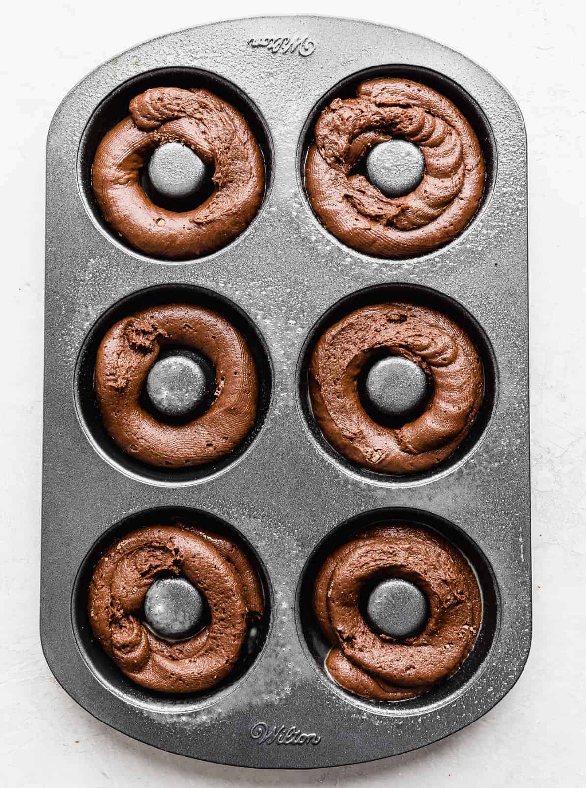A donut pan with chocolate batter in each donut cavity.