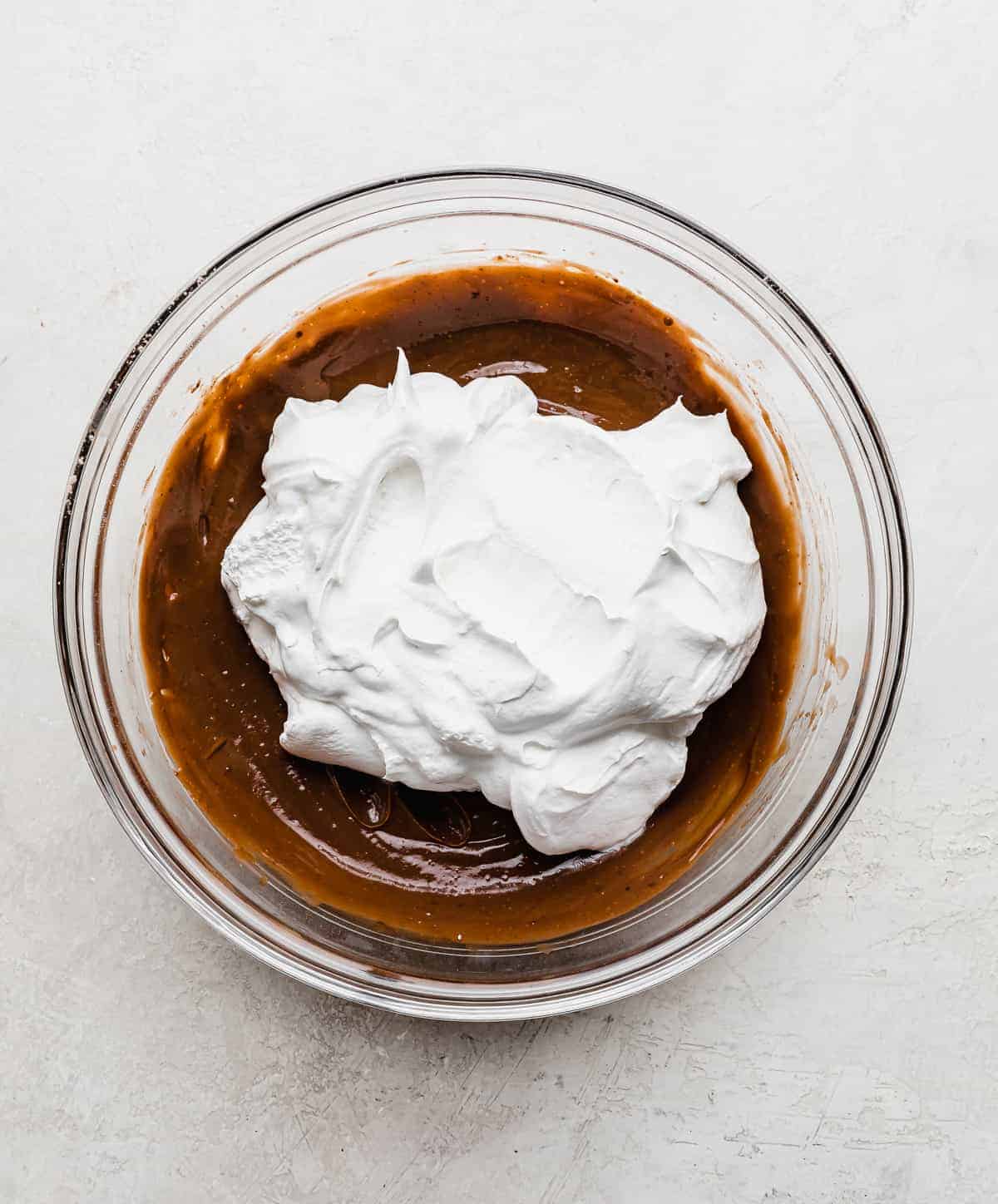 Whipped cream on top of brown chocolate pudding in a glass bowl.