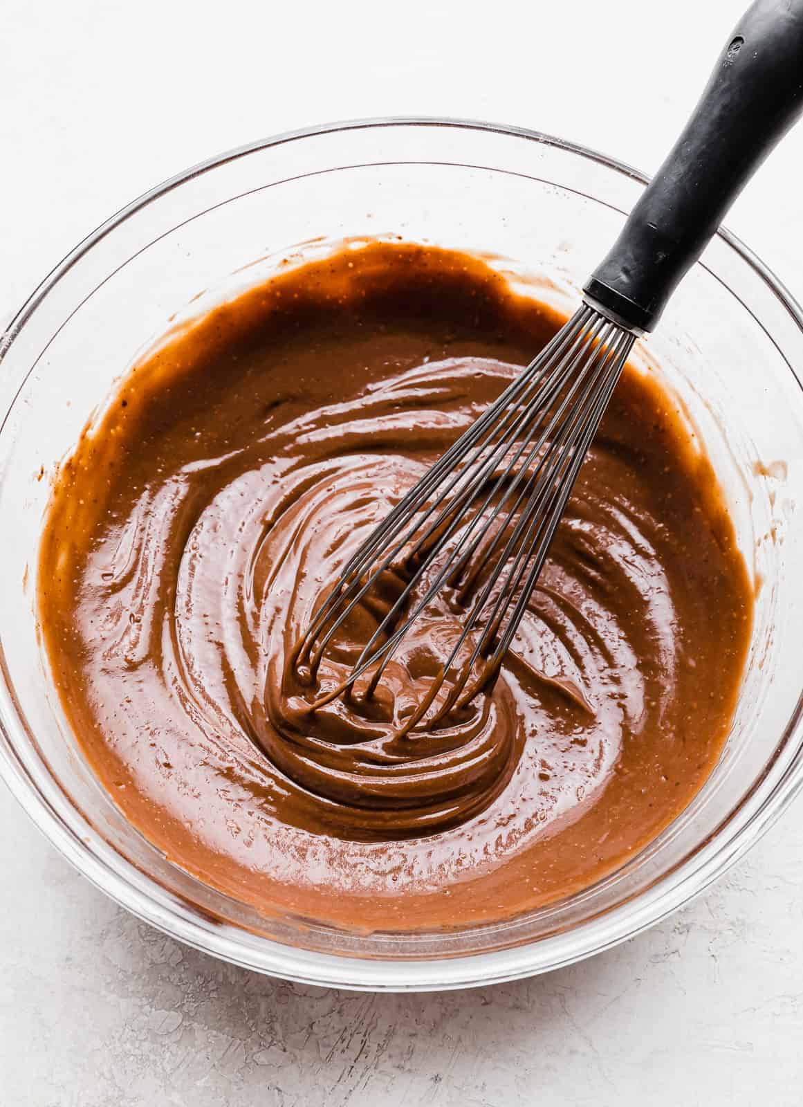 A whisk stirring chocolate pudding a glass bowl.