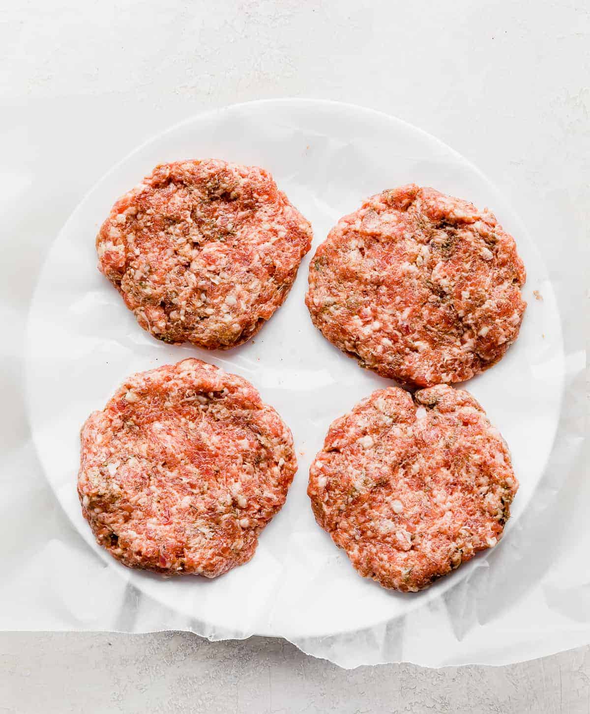 Four raw sausage patties on a white plate.