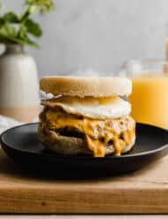 Homemade Sausage and Egg McMuffin on a black plate with orange juice in the background.