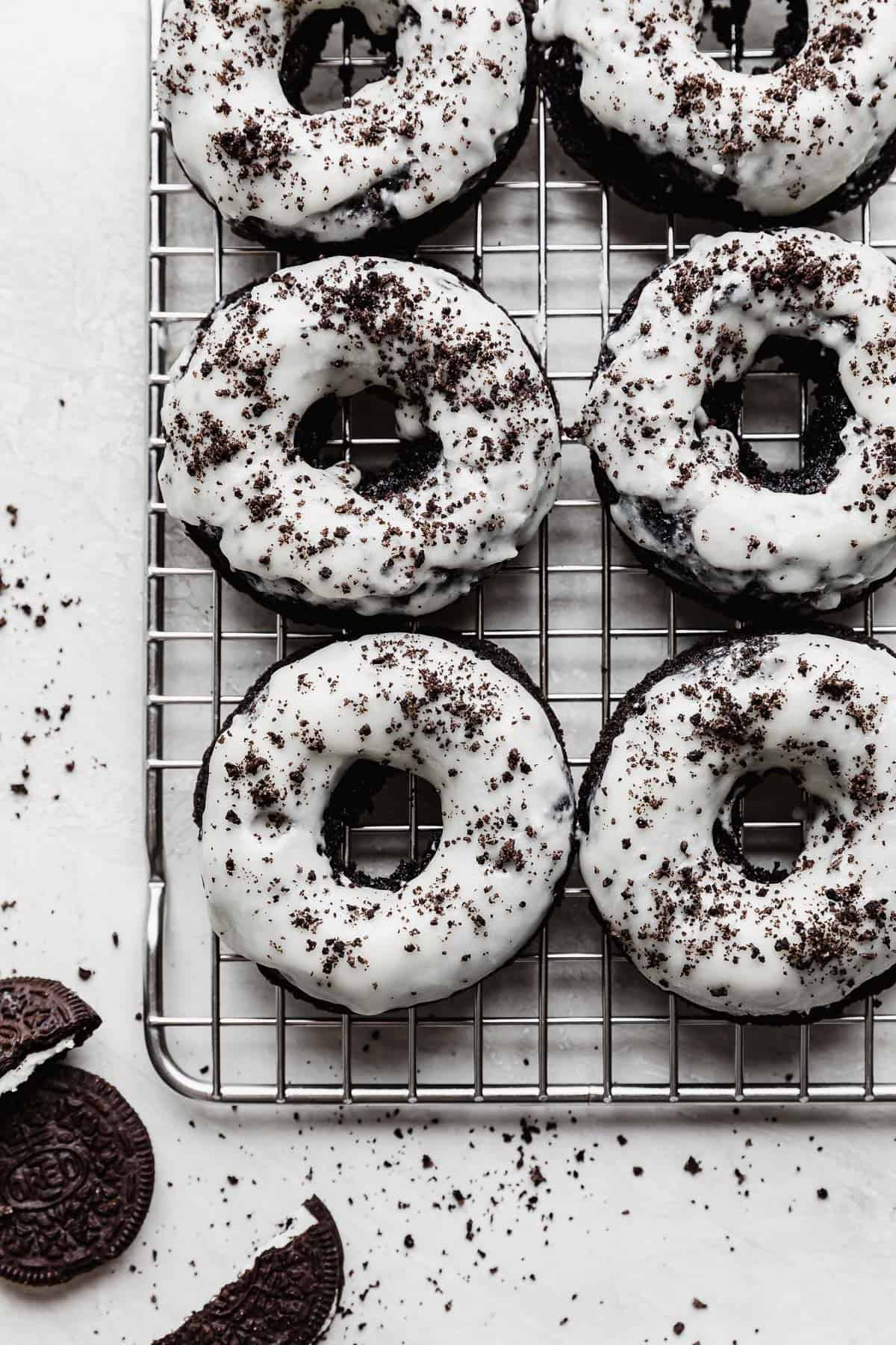 White frosting topped Oreo Donuts with Oreo crumbs overtop, on a wire rack.