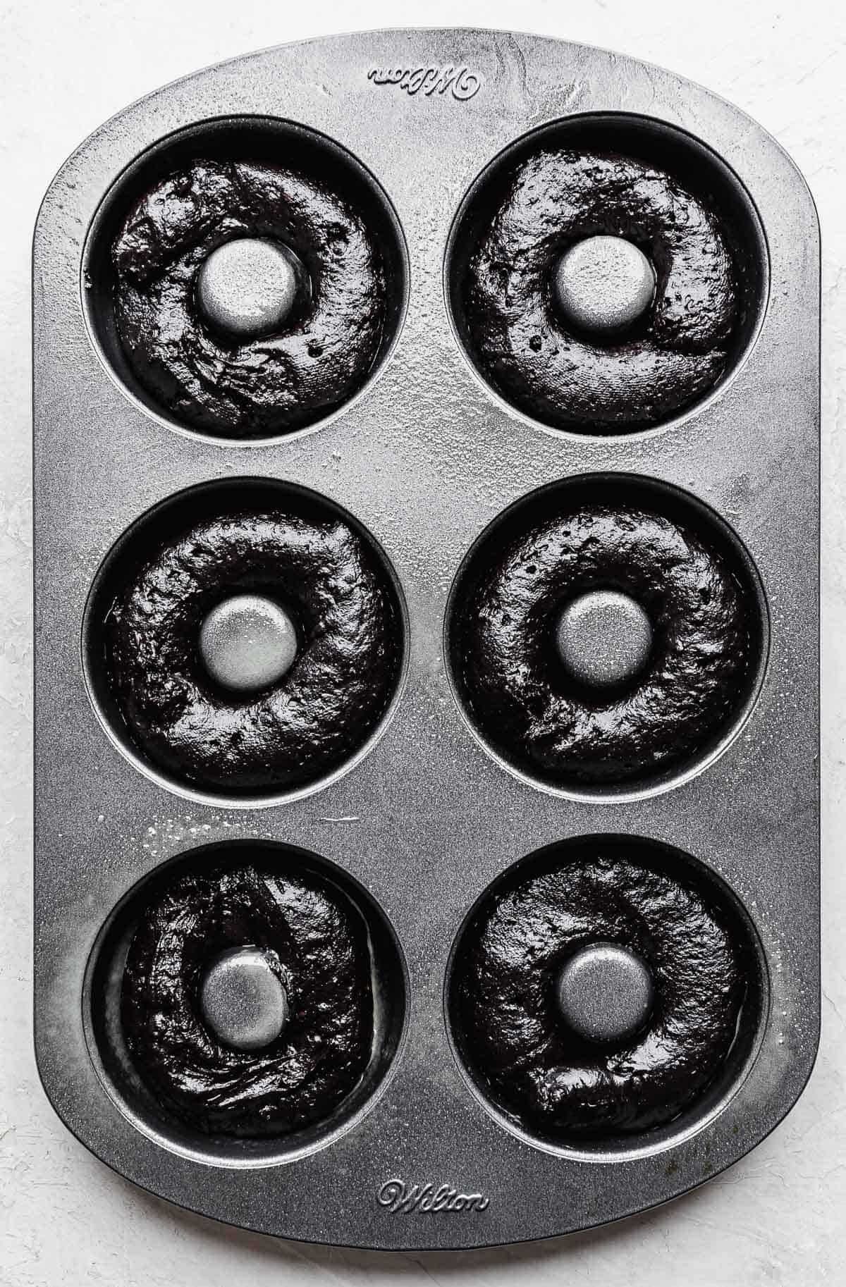 Oreo Donut batter in a six cavity donut pan on a white background.