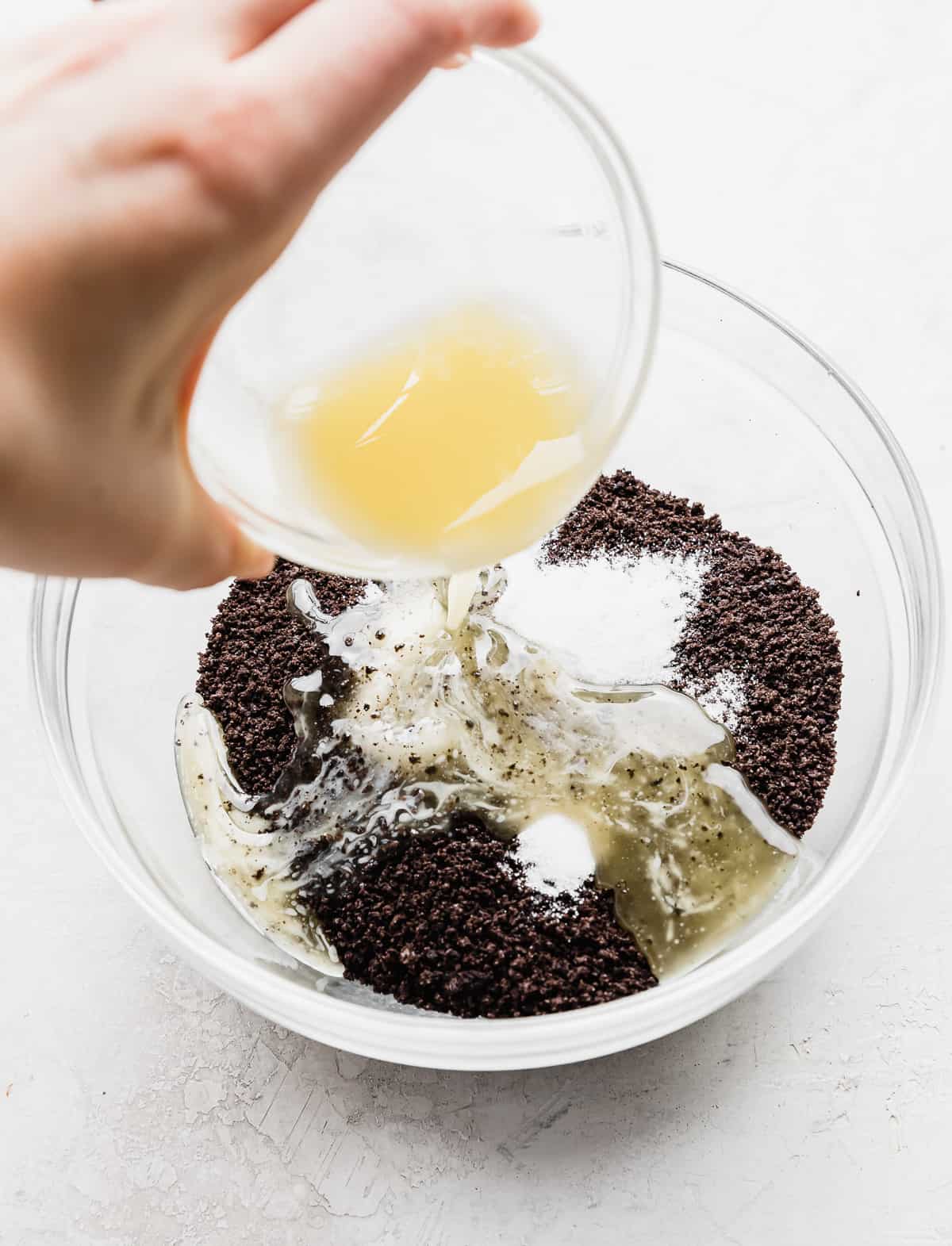 Melted butter being poured into a bowl full of crushed Oreo crumbs and sugar.
