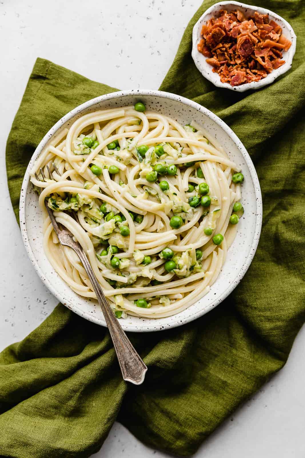 A white plate with Pasta with Zucchini Sauce and green peas.