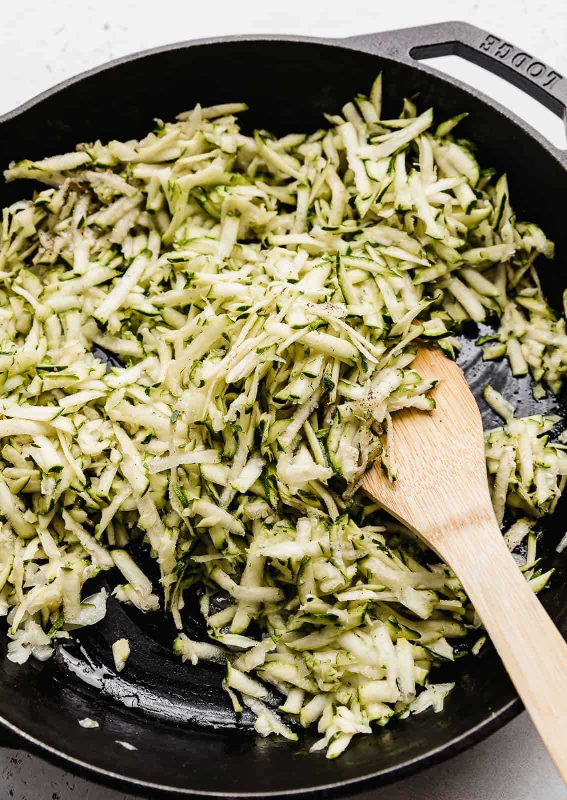 Close up photo of shredded zucchini in a black skillet.