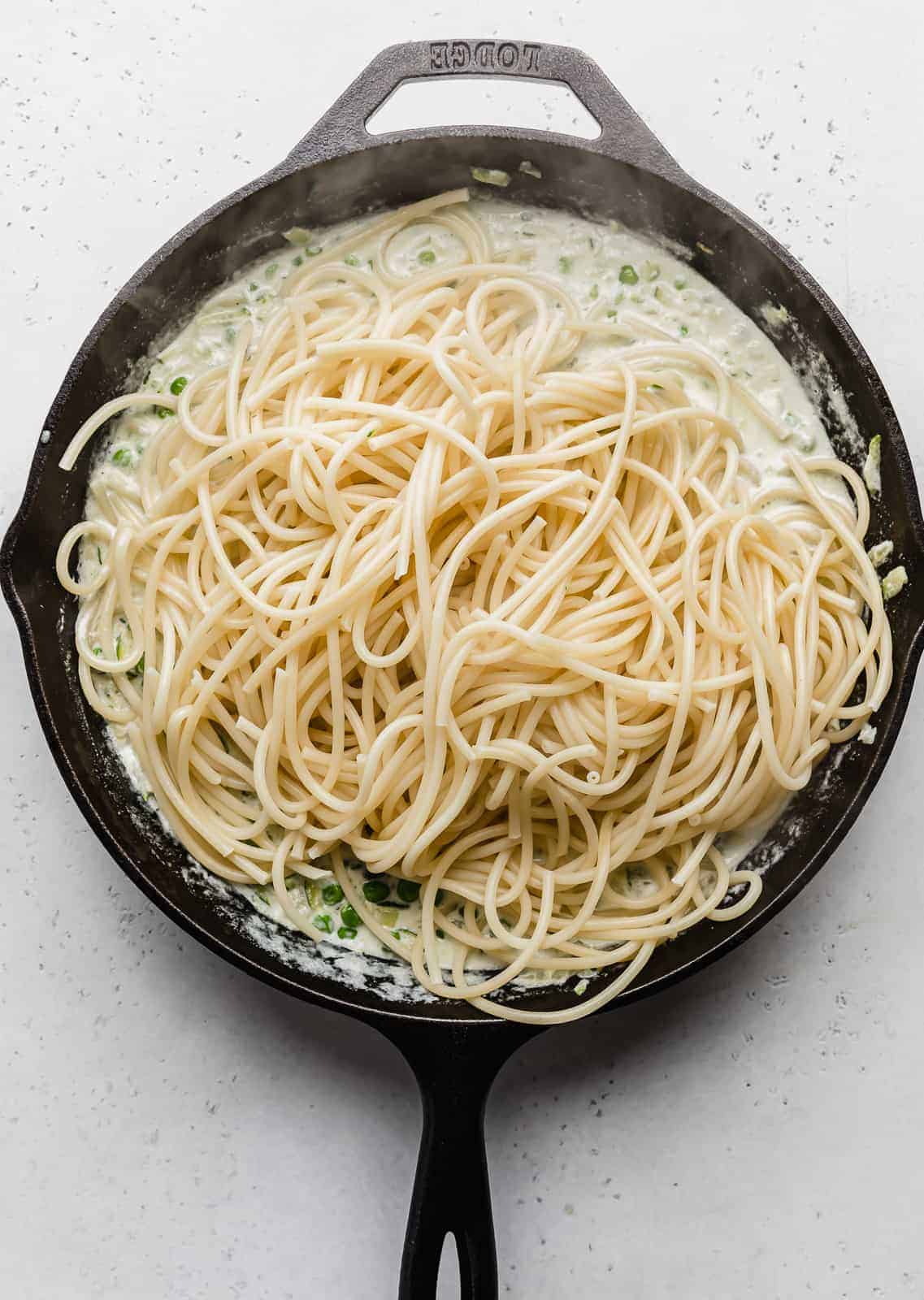 A black skillet with cooked bucatini noodles atop a zucchini sauce.