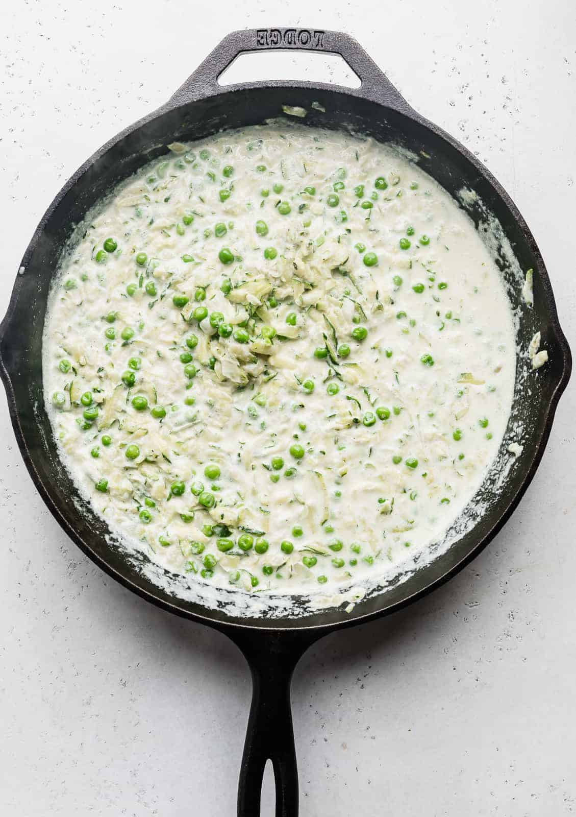 A black skillet with shredded zucchini in a white sauce.