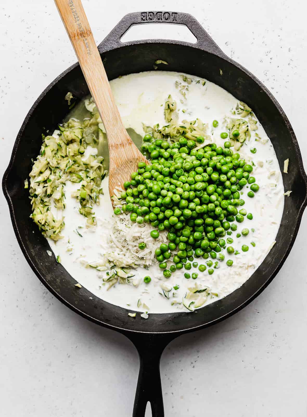 A skillet full of frozen peas, shredded zucchini, and a white sauce.