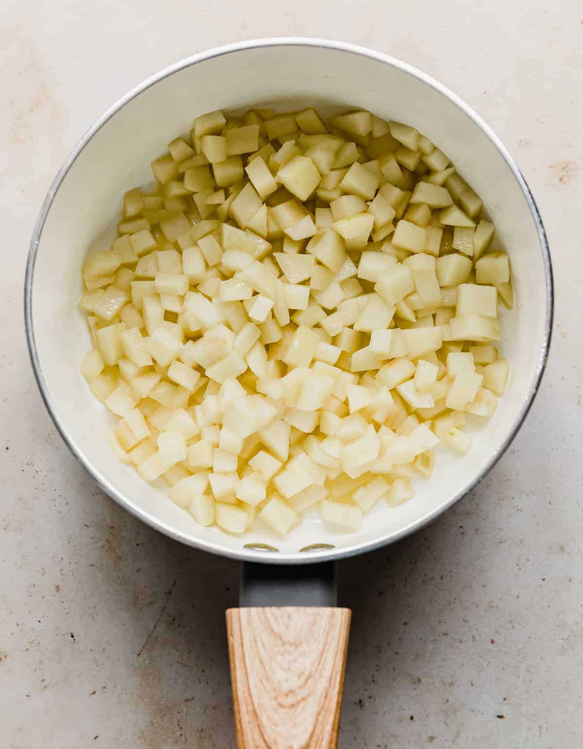 Softened diced apples in a white saucepan.