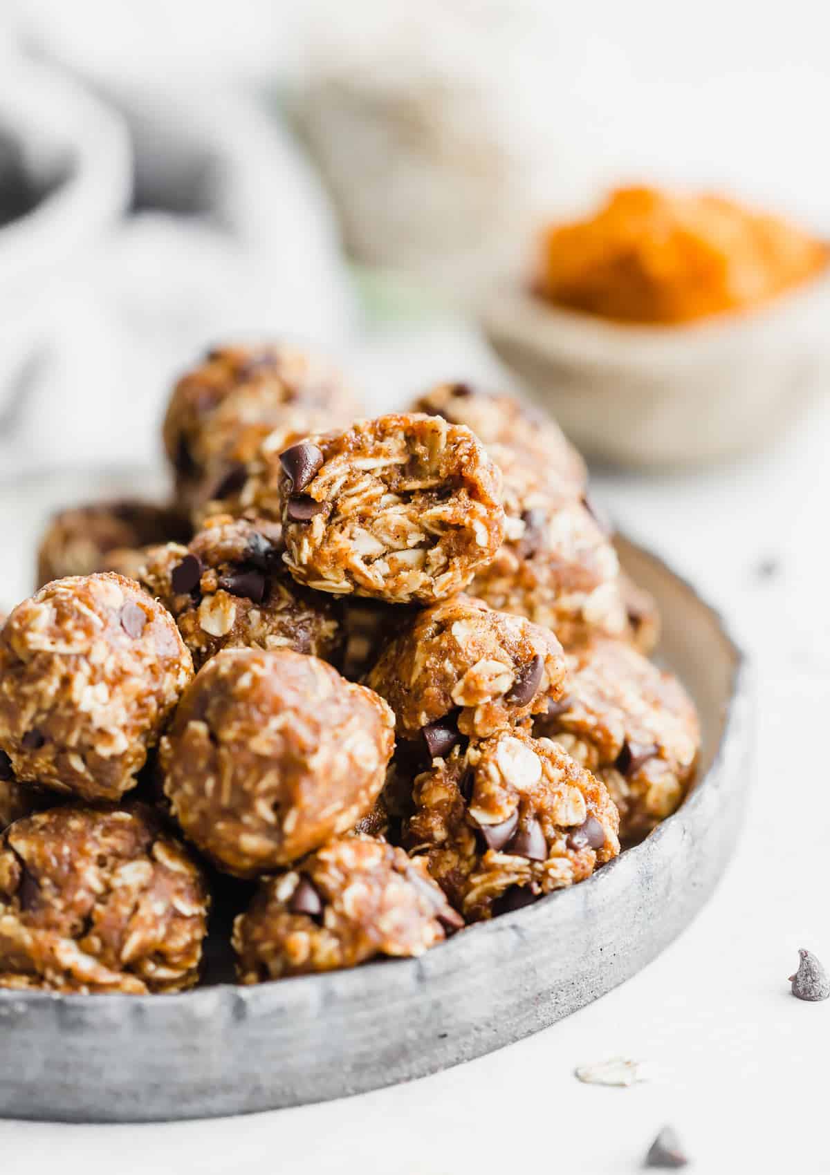 A stack of Pumpkin Energy Balls on a plate with pumpkin puree in the background. 